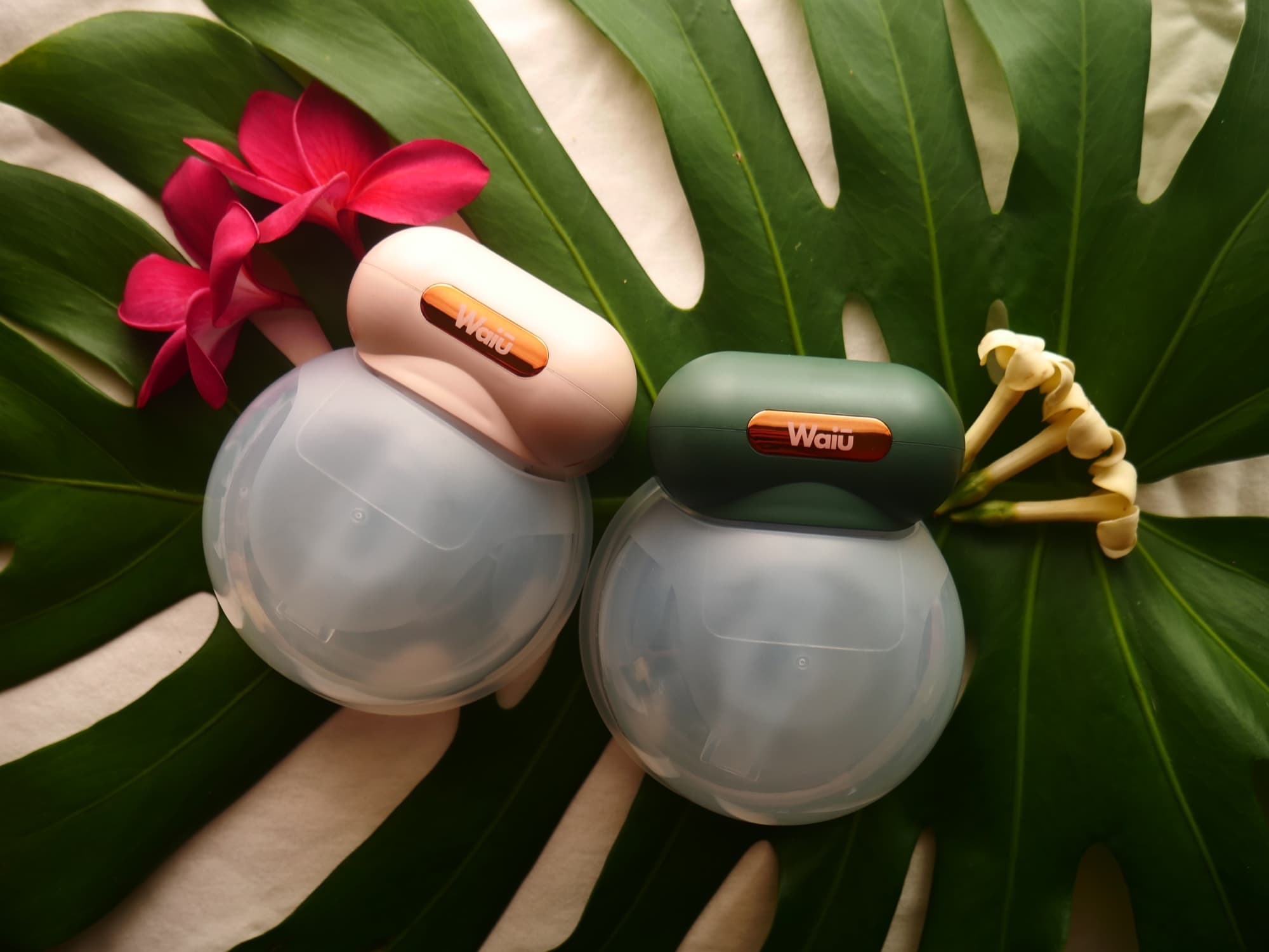 Two Waiū wearable breast pumps arranged on green tropical leaves with flowers