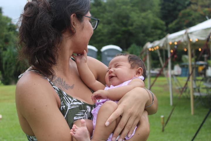 A mother smiling toward the baby she is holding outdoors